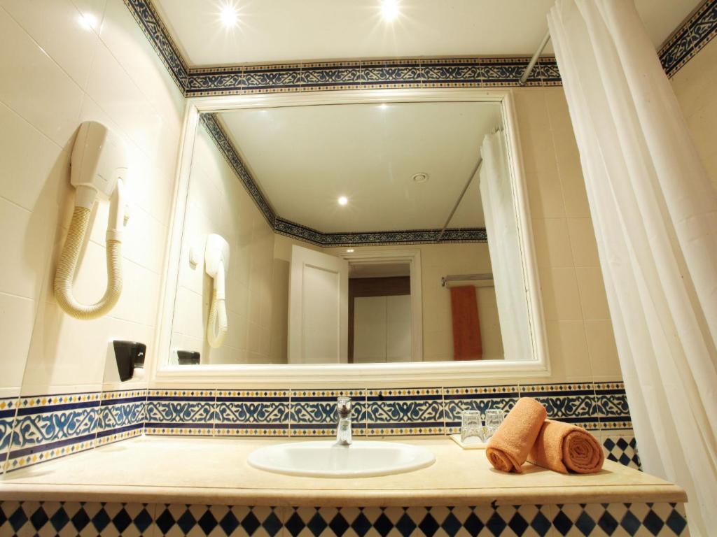 Vannas istaba ar modernu dizainu, spoguli un krāsainu flīžu apdari. Uz izlietnes ir novietotas dvieļi un glāzes.