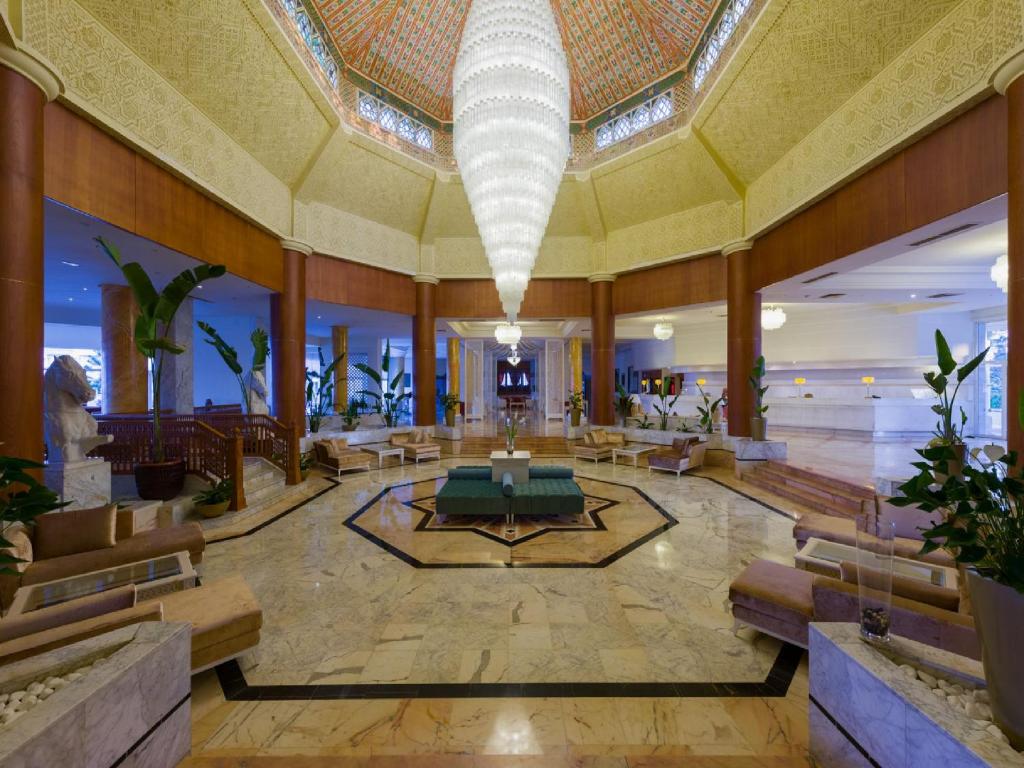 Greznas viesnīcas vestibilis ar augstām griestiem, izsmalcinātu apgaismojumu un mūsdienīgu interjeru, kas ietver zaļas augu kompozīcijas un ērtas sēdvietas.