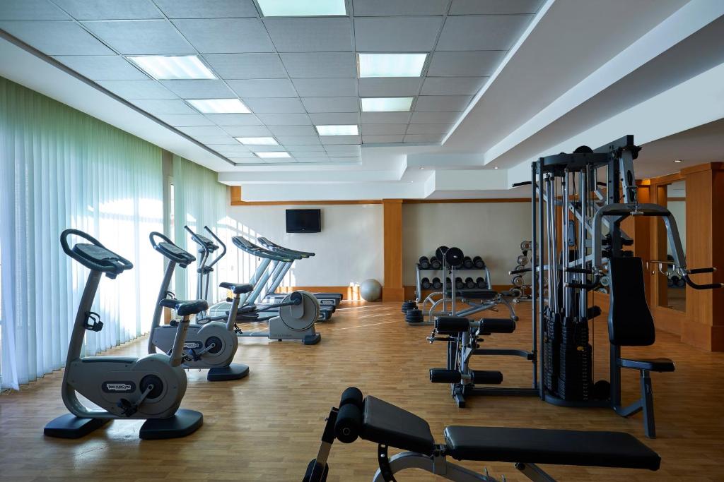 Mūsdienīgs sporta zāles interjers ar dažādām fitnesa iekārtām un trenažieriem, gaismas plūstošs caur lielajiem logiem.