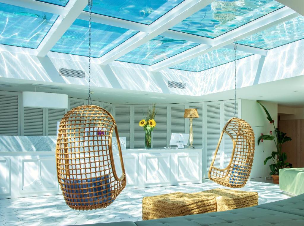 Mūsdienīgs interjers ar šūpošanos no ratiņiem un stikla jumtu, caur kuru redzams ūdens. Gaisma spēlējas uz grīdas, radot relaksējošu atmosfēru.