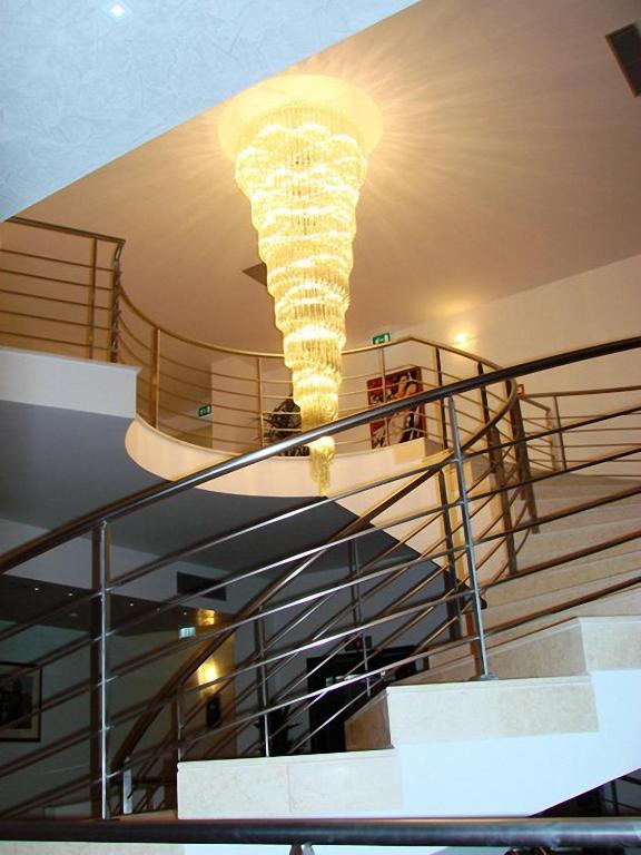 Elegants interjers ar spirālveida lustru, kas karājas virs kāpnēm, radot mūsdienīgu atmosfēru. Kāpņu margas un gaišas sienas papildina telpas estētiku.
