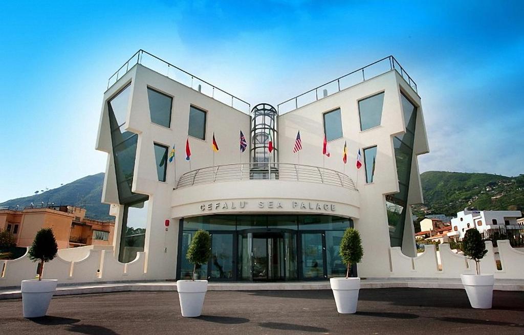 Mūsdienīga arhitektūra, kas attēlo Cefalū jūras pili, ar izteiksmīgām formām un daudzām karogiem. Šī ēka atrodas gleznainā kalnu ainavā.