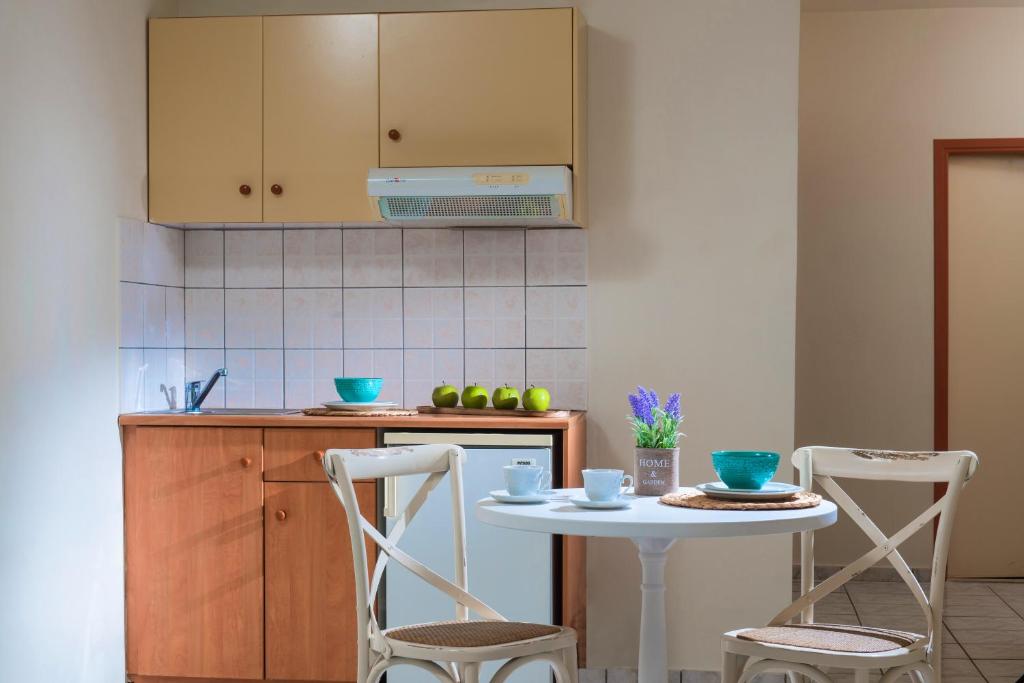 Kompaktā virtuve ar koka mēbelēm un gaišām flīzēm, kurā redzami trīs zaļi āboli un ziedi vāzē uz galda. Ideāla vieta mājīgām brokastīm vai ģimenes sanākšanai.