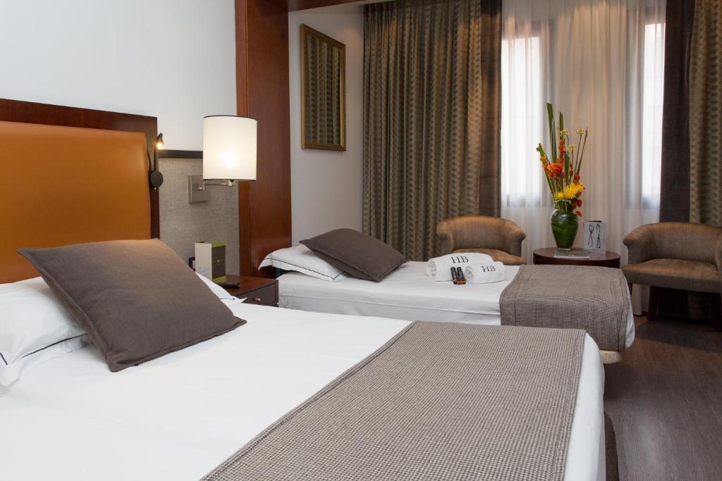 Mūsdienīgs viesnīcas numurs ar diviem gultām, brūnu spilvenu un elegantu interjeru, kas ietver dīvānus un puķu kompozīciju. Ideāla vieta atpūtai un relaksācijai.