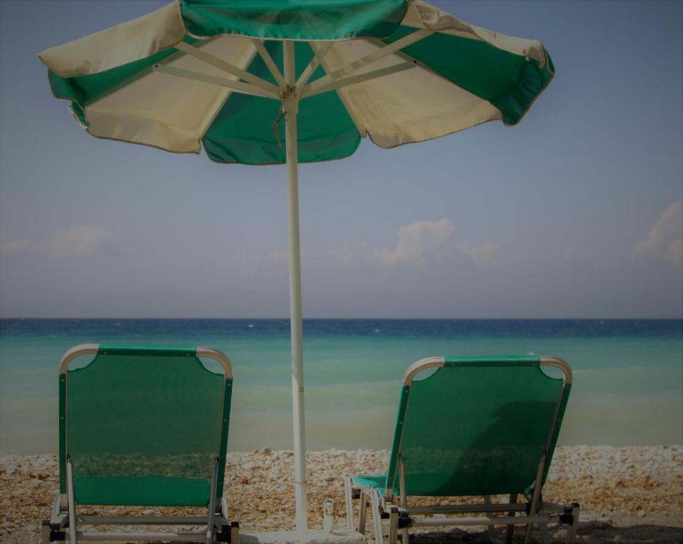 Pludmales krēsli zem zaļas un baltas saulessargu, ar skatu uz mierīgu jūru un debesīm. Ideāls brīvdienu atmosfēras attēls.