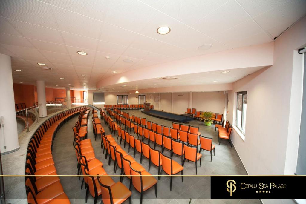 Konferences zāle ar oranžām krēsliem un skatu uz skatuvi. Telpa ir gaiša un moderna, piemērota sanāksmēm un pasākumiem.