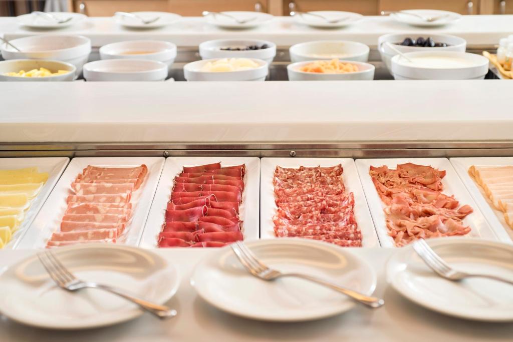 Svaigu gaļas un siera šķēļu izvēle uz bufetes galda, ar daudzām garnelēm un salātiem fonā.