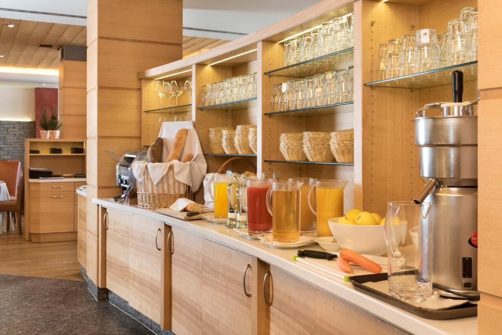 Brokastu bufete ar dzērieniem un cepumiem, kas pasniegti modernā, koka interjerā. Kafijas automāts un augļu trauki papildina viesnīcas atmosfēru.