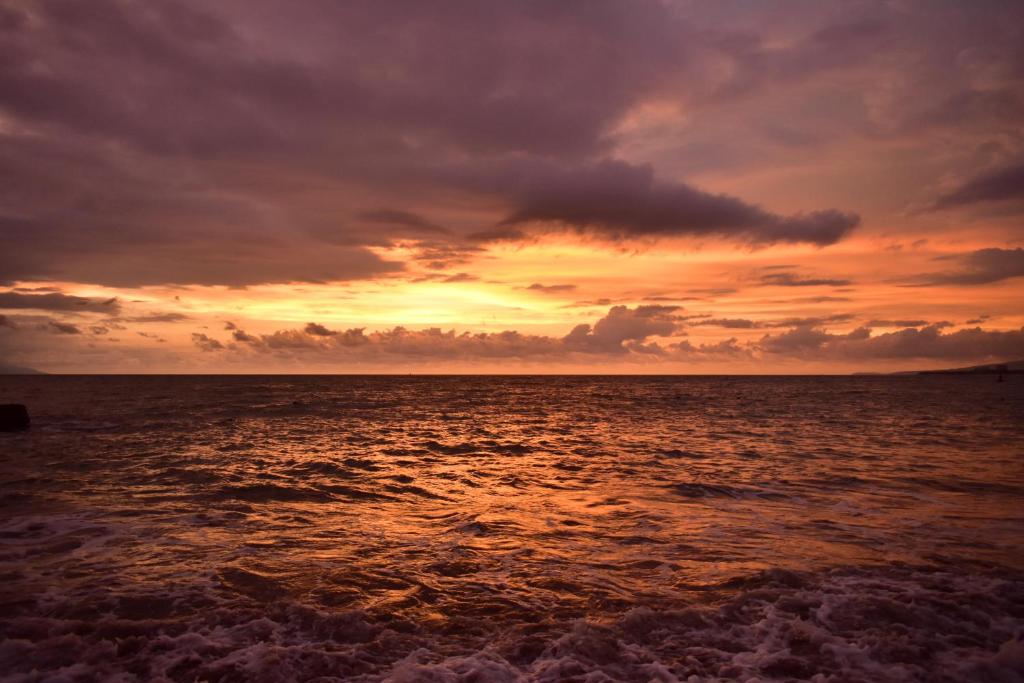 Saulriets pār jūru, ar krāsainiem mākoņiem un viļņiem, kas sitas krastā. Dabas ainava, kas rada mierīgu un skaistu atmosfēru.
