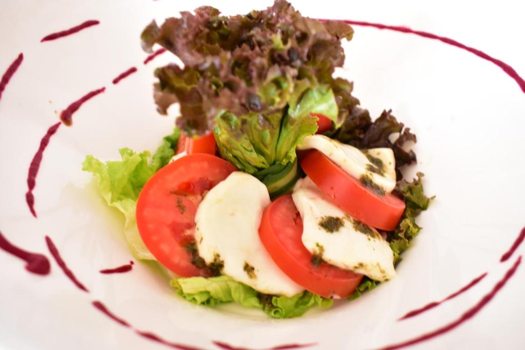 Svaiga salātu kompozīcija ar tomātiem, mocarellu un zaļumiem, dekorēta ar salātiem un mērci.