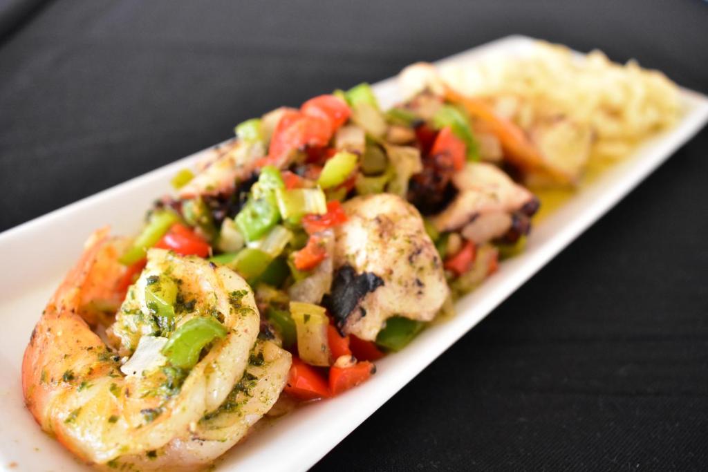 Garšīgi cepti garneles un vistas gaļa ar dārzeņiem, pasniegti uz šauras balta šķīvja. Ideāls ēdiens, kas apvieno krāsainus dārzeņus un sulīgu gaļu.