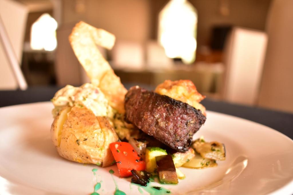 Skaisti pasniegts gaļas ēdiens ar ceptu kartupeli un dārzeņiem, izrotāts ar krāsainu mērci.