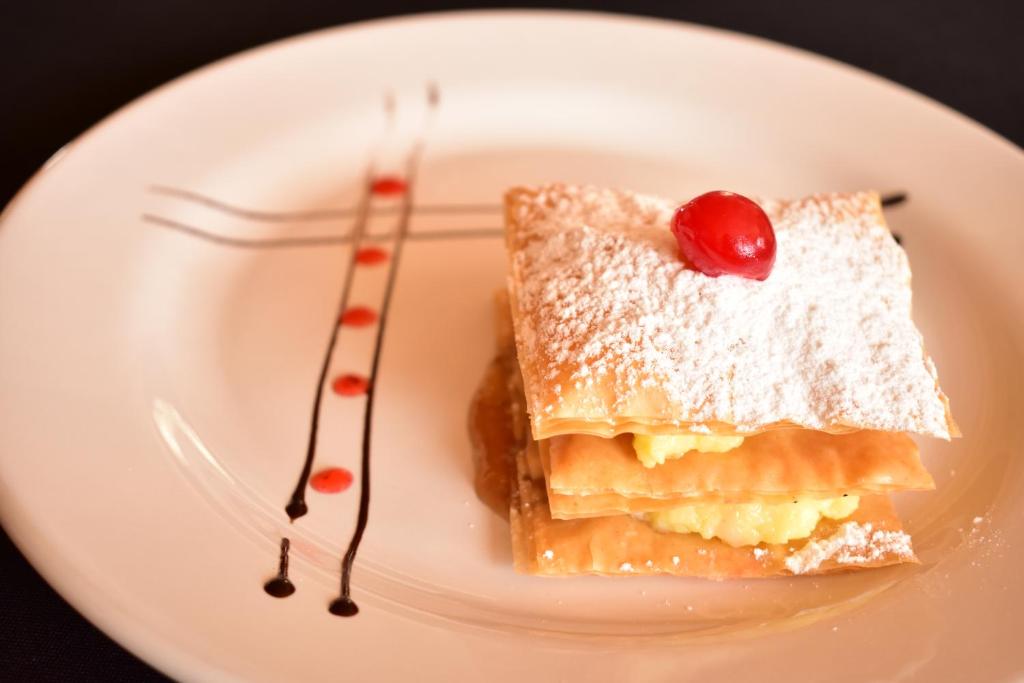 Klātesošs deserts ar kārtainās mīklas slāņiem, pildīts ar krēmīgu sastāvdaļu un apkaisīts ar pūdercukuru, dekorēts ar ķiršu.