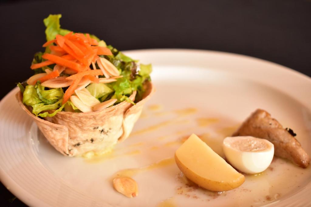 Svaiga salātu porcija, pasniegta kraukšķīgā maizes kausā, ar burkānu un mandelēm, blakus ir vārīta ola un kartupeļa šķēle.