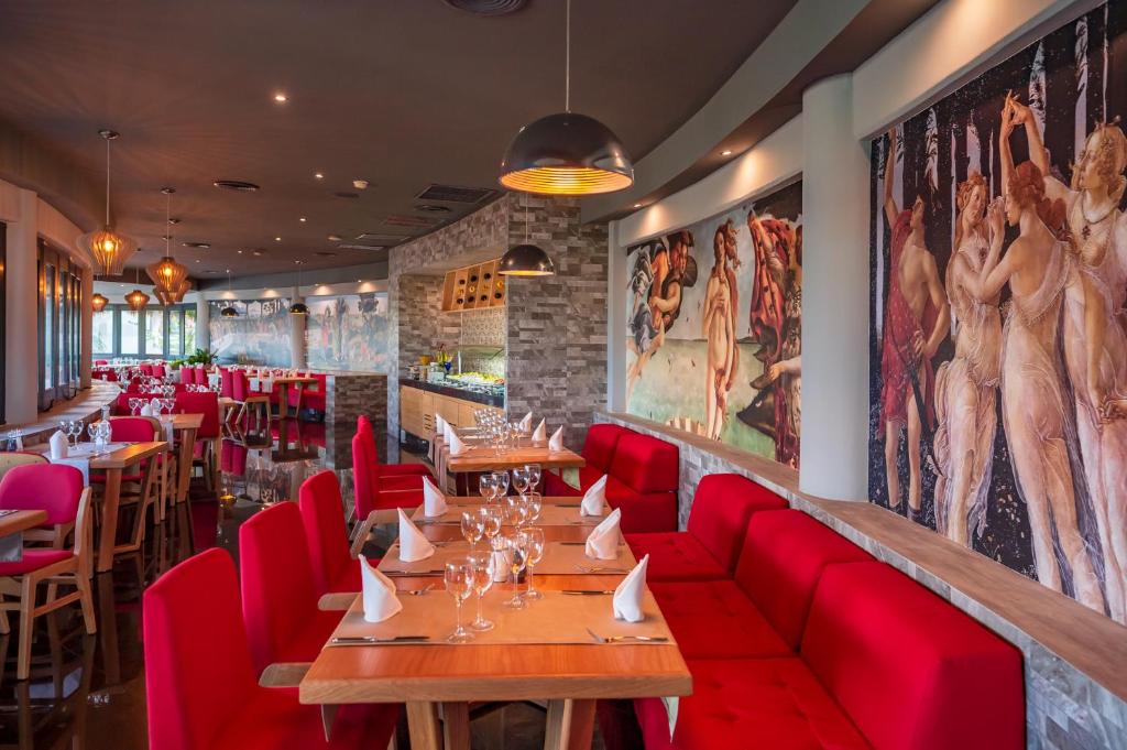 Mūsdienīgs restorāns ar elegantu interjeru, sarkaniem krēsliem un gleznām uz sienām, kas rada patīkamu atmosfēru. Galdi ir sakārtoti ar glāzēm un salvetēm, gatavi viesu uzņemšanai.