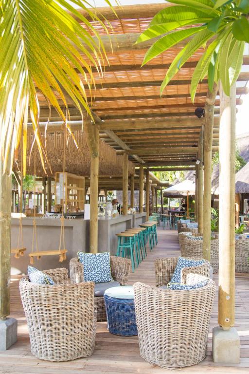 Viesmīlīga terase ar vītņu krēsliem un zilu galdu, kas atrodas zem koka nojumes, radot relaksējošu atmosfēru. Ideāla vieta, lai izbaudītu laiku brīvā dabā.