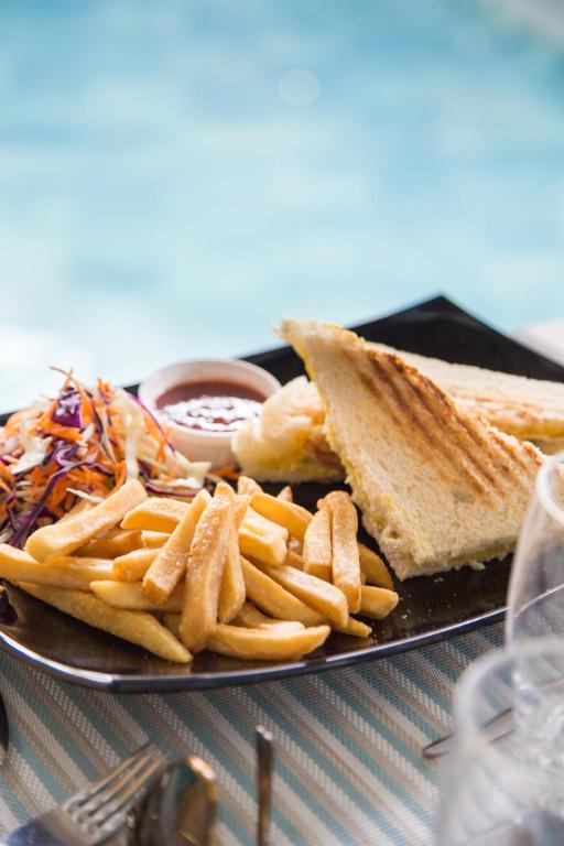 Svaigās sviestmaizes ar frī kartupeļiem un salātiem, pasniegtas uz melnas šķīvja, fona redzams peldbaseins.