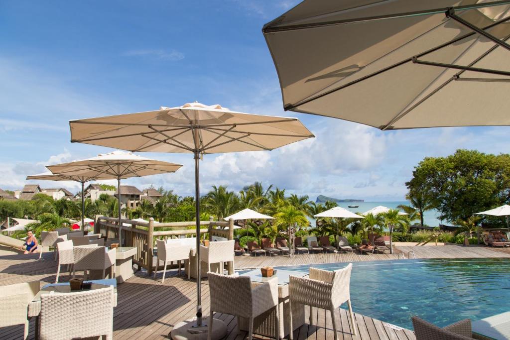 Kārdinēta atpūtas zona ar baseinu, kurā ir terase ar saulessargiem un pludmales krēsliem, ieskauta zaļumiem un ar skatu uz jūru.