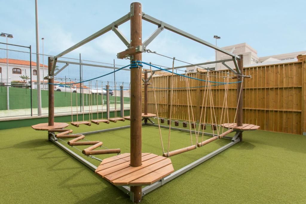 Bērnu spēļu laukums ar šķēršļu trasi, kas sastāv no koka platformām un virvēm, uz zaļā zāliena. Ideāls vieta bērnu aktivitātēm un fiziskajai attīstībai.