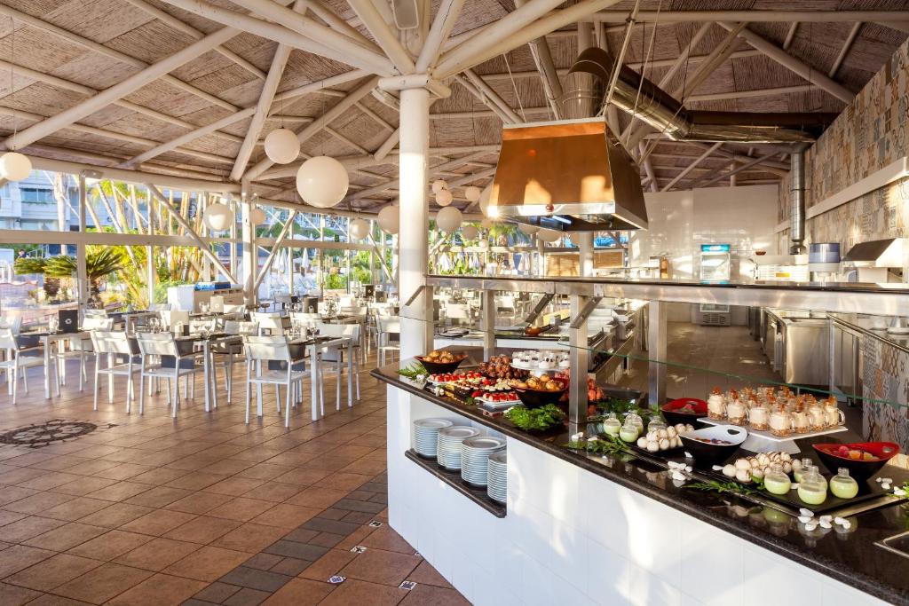 Moderns restorāns ar atvērtu virtuvi, kas piedāvā plašu ēdienu izvēli, iekārtots ar gaišām krāsām un elegantiem galdiem. Gaismas un zaļumi rada patīkamu atmosfēru.