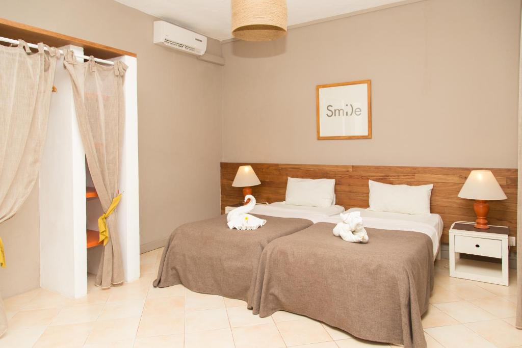 Mūsdienīga viesnīcas numura iekārtojums ar divām gultām, siltām krāsām un dekoratīvām dvieļu figūrām. Telpā ir gaisma un mīksts apgaismojums, radot mājīgu atmosfēru.