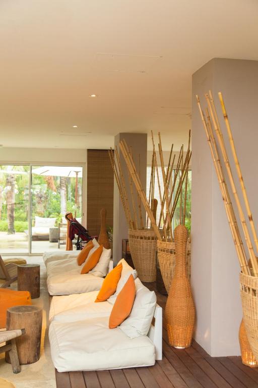 Mūsdienīgs interjers ar komfortablām baltām dīvāna vietām, oranžām spilvenēm un bambusa dekorācijām, radot relaksējošu atmosfēru. Iekštelpu telpa ar lieliem logiem, kas ved uz dārzu.