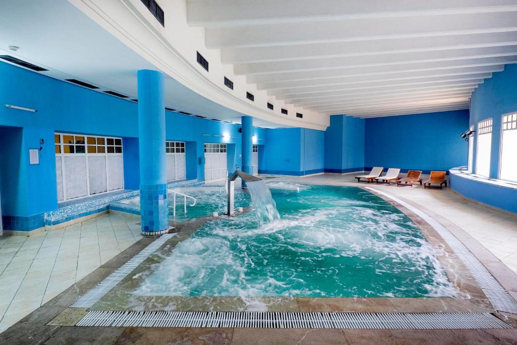 Relaksējoša iekštelpu peldbaseina un spa zona ar zilām sienām, burbuļojošu ūdeni un atpūtas krēsliem. Ideāla vieta atpūtai un relaksācijai.