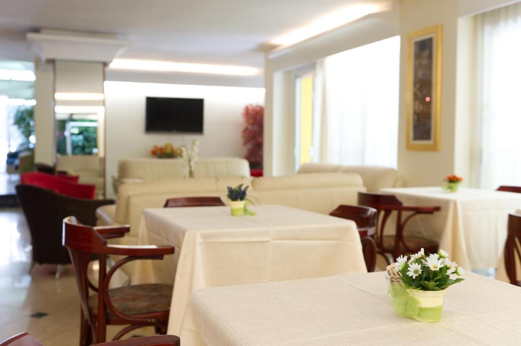 Mūsdienīgs un gaišs interjers ar galdiem, ziedu kompozīcijām un mīkstajām mēbelēm, radot patīkamu atmosfēru.