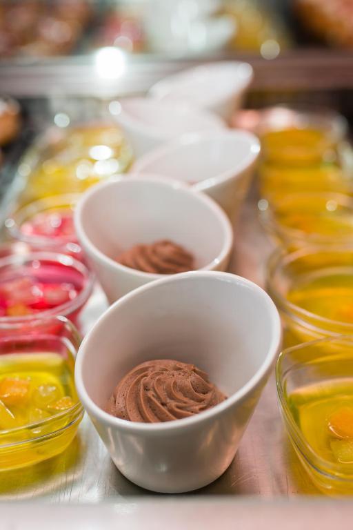 Bļodiņās redzams šokolādes krēms un dažādas krāsainas želejas deserti, radot pievilcīgu saldumu galdu.