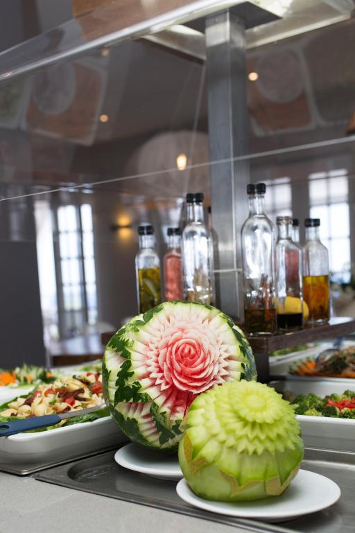 Skaisti izgrebti arbūzi un melone, kas izkārtoti uz galda, blakus garšīgu ēdienu izvēlei un dzērienu pudelēm.