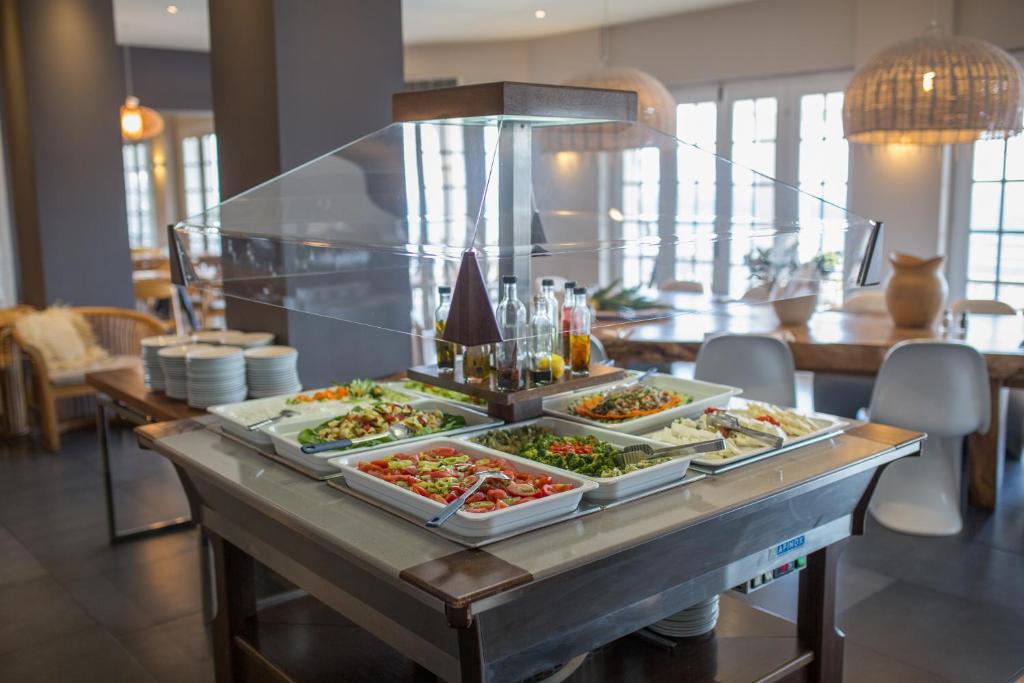 Svaigu salātu bufete ar dažādām dārzeņu un salātu opcijām, kas pasniegta modernā restorāna interjerā. Pusdienu galds ir dekorēts ar elegantām šķīvju un trauku kārtām.