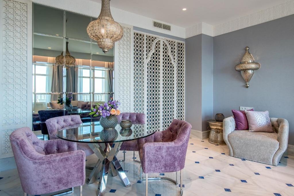 Mūsdienīga ēdamzona ar elegantiem rozā krāsas krēsliem un stikla galdu, dekorēta ar ziediem un gaismas ķermeņiem. Interjerā ir izmantoti smalki raksti un spoguļi, radot plašuma un gaismas sajūtu.