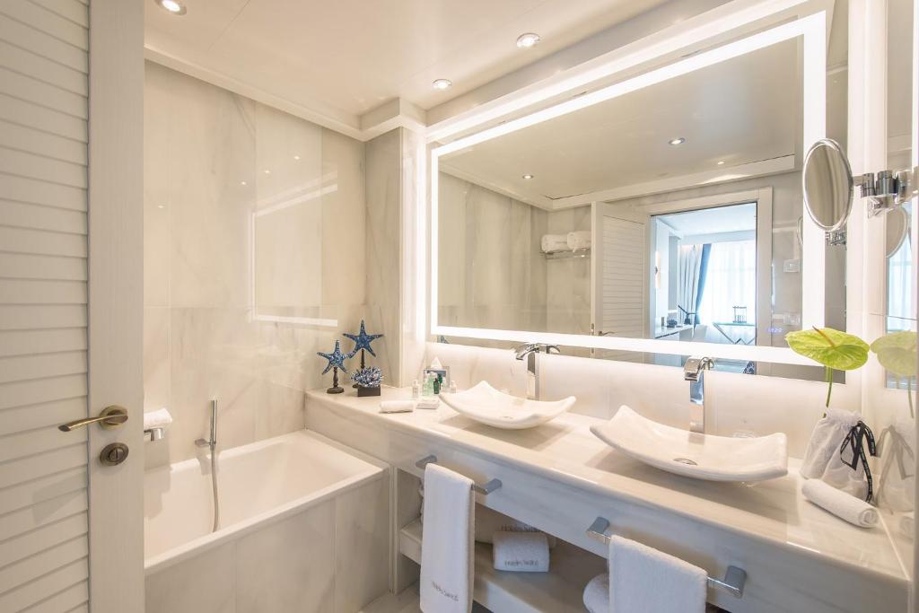 Mūsdienīgs vannas istabas interjers ar divām izlietnēm, vannu un gaismas spoguli, papildināts ar dekoratīviem elementiem. Eleganta, gaiša atmosfēra ar marmora sienām un stilīgām detaļām.