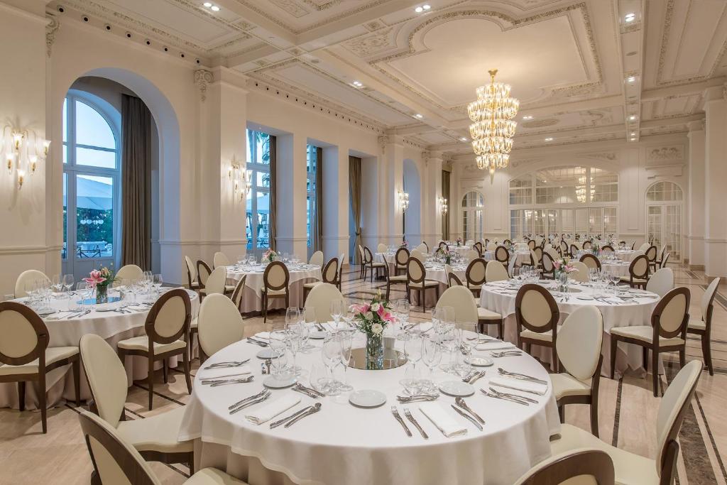 Elegants restorāns ar izsmalcinātu interjeru, kas ietver apaļus galdus, greznas krēslus un dekoratīvas gaismas. Telpa ir piepildīta ar dabīgu gaismu un rotāta ar ziedu kompozīcijām.