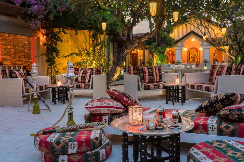 Skaisti dekorēta āra atpūtas zona ar krāsainām spilveniem un šašlikiem, kas apgaismota ar siltām gaismām, radot relaksējošu atmosfēru.