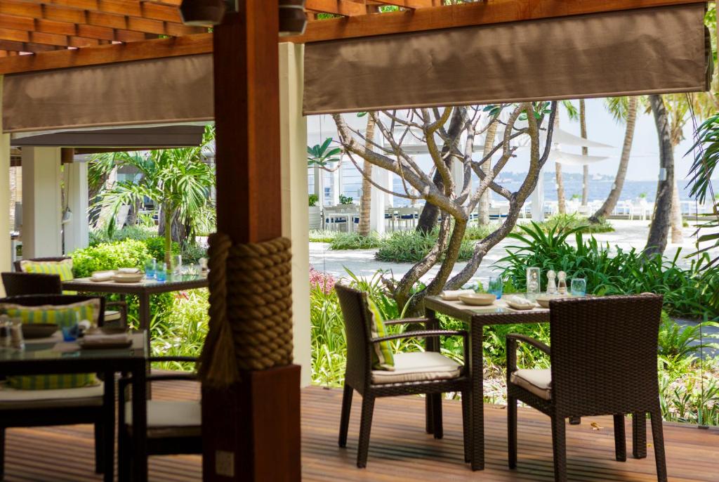 Āra restorāna terase ar ērtām krēsliem un galdiem, apkārtne apzaļumota ar palmām un krūmiem, radot relaksējošu atmosfēru.