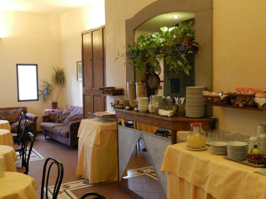 Kafejnīca ar mājīgu interjeru, kurā redzami galdi ar dzeltenām galdautām, komfortablas dīvāni un bufete ar dažādiem ēdieniem un dzērieniem.