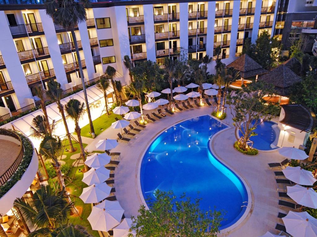 Elegants viesnīcas pagalms ar baseinu, ap kuru izvietoti saules krēsli un lietussargi, kā arī zaļi augi un koki. Vakarā apgaismots, radot relaksējošu atmosfēru.