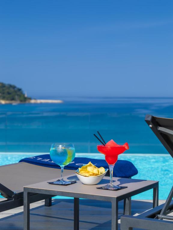 Dzertuves un čipsi uz galda pie baseina ar skatu uz jūru, ideāla vieta relaksācijai un atpūtai.