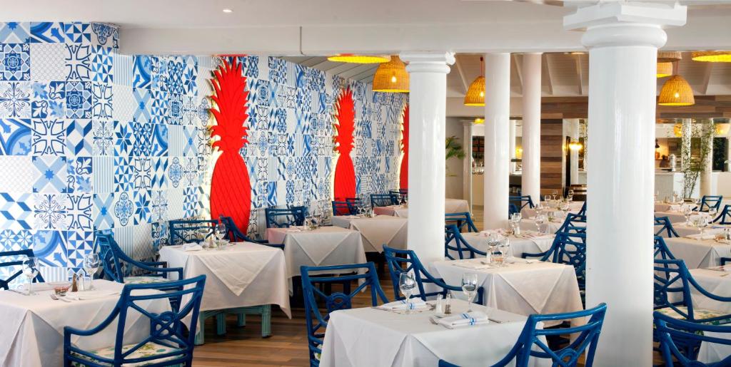 Restorāna interjers ar zilu un baltu keramikas flīžu sienu, kas papildināta ar sarkanu ananāsu motīvu. Galdi ir klāti ar baltām galdautām, un zilu krēslu rinda rada patīkamu atmosfēru.