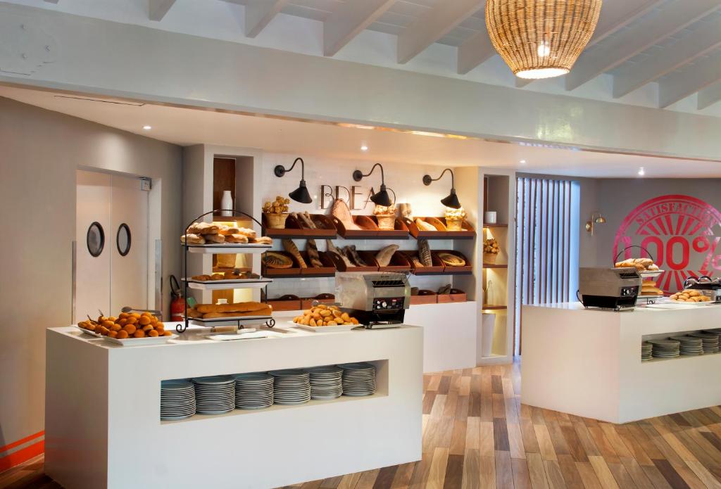 Moderns bistro interjers ar plašu maizes klāstu un elegantām apgaismojuma lampām. Uz galda redzami dažādi cepti izstrādājumi un trauki.