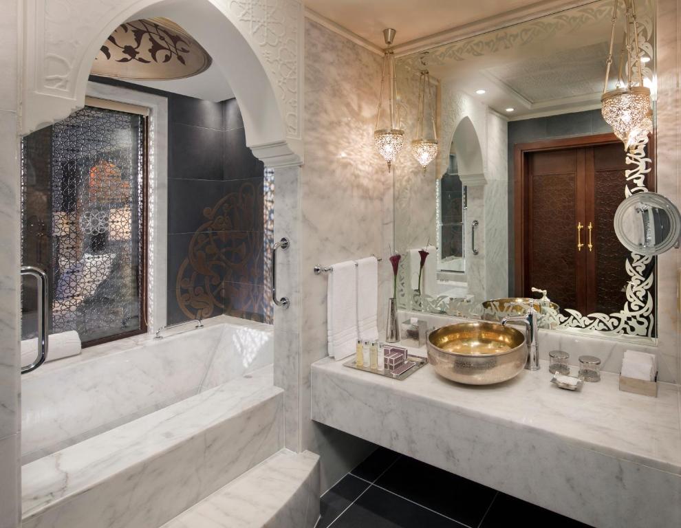 Mūsdienīgs vannas istabas interjers ar marmora apdari, dekoratīvām lampām un elegantu spoguli. Izceļas vannas un dekoratīvie elementi, radot relaksējošu atmosfēru.