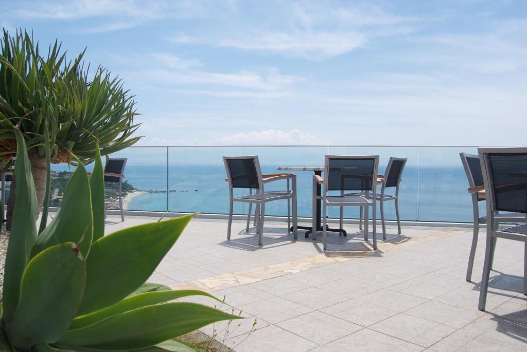 Terase ar skatu uz jūru, kurā ir koka galdi un krēsli, apstādīta ar zaļām augu kompozīcijām. Ideāla vieta relaksācijai un baudīšanai.