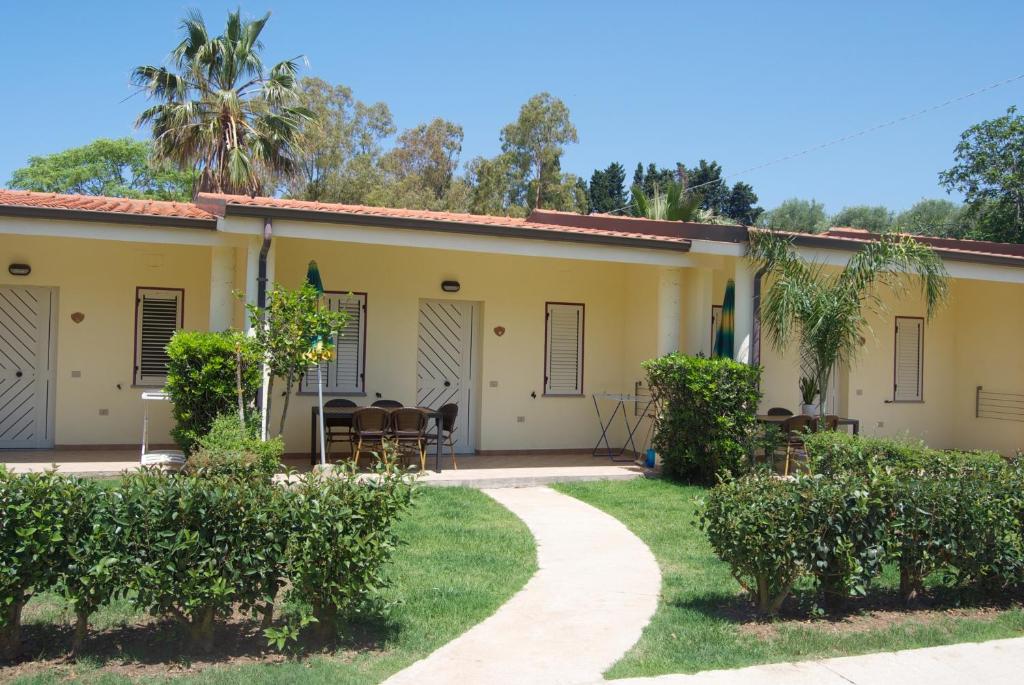 Vasaras māju komplekss ar dārzu un terasi, kurā ir galdi un krēsli. Apkārt ir zaļumi un palmas, radot relaksējošu atmosfēru.