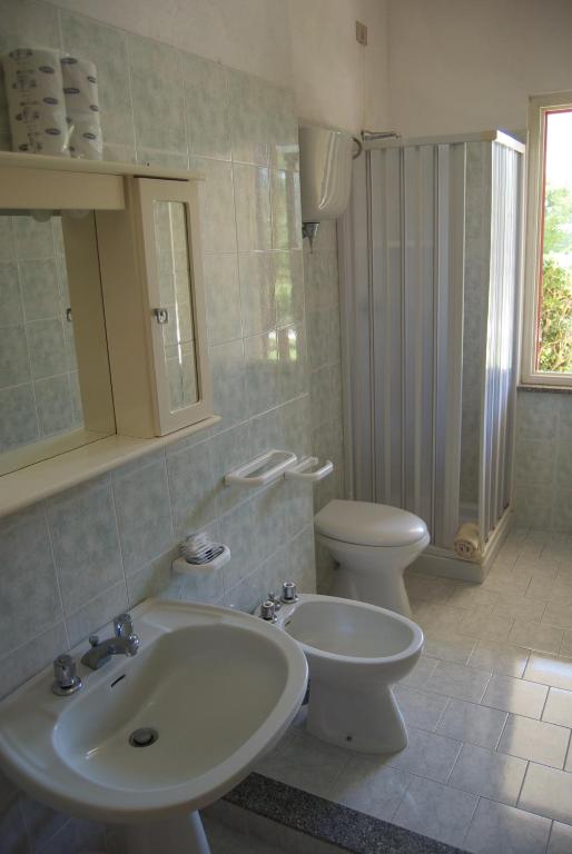 Mājas vannas istaba ar gaišiem flīzēm, dušas kabīni, tualeti un izsistītu spoguli. Telpa ir gaiša un tīra, ar logu, kas sniedz dabisko apgaismojumu.