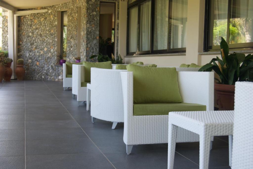 Terases zona ar baltām mēbelēm un zaļiem spilveniem, kas izvietotas uz akmens sienas fona. Ideāla vide relaksācijai un atpūtai.