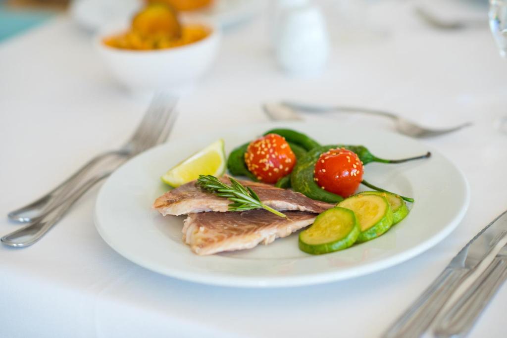 Garšīgi pasniegts cepts zivs fileja ar svaigiem dārzeņiem, citronu un rozmarīnu uz balta šķīvja. Ideāls ēdiens veselīgas maltītes baudīšanai.
