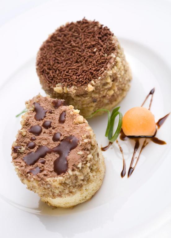 Šokolādes deserts ar riekstiem un dekoratīvu meloni, kas pasniegts uz balta šķīvja.