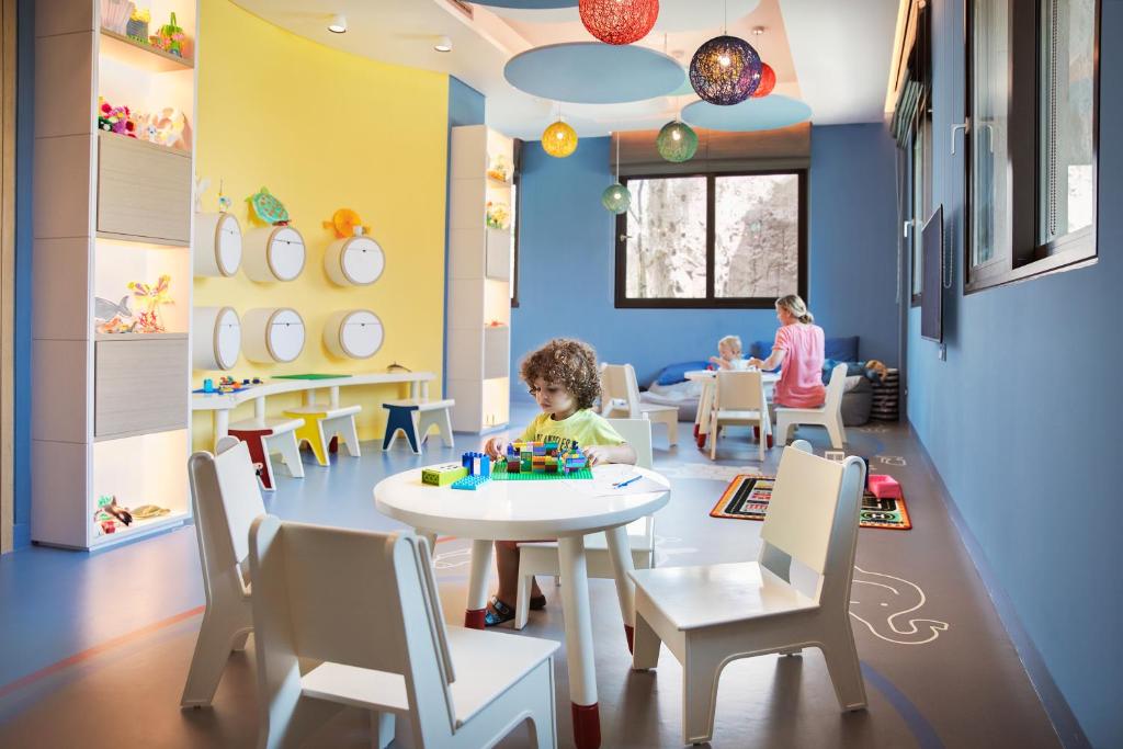 Bērnu istaba ar spilgtām krāsām, kur bērni spēlējas ar LEGO un citiem radošiem spēļlietu komplektiem. Telpā ir arī ērtas bērnu mēbeles un dekoratīvas gaismas.