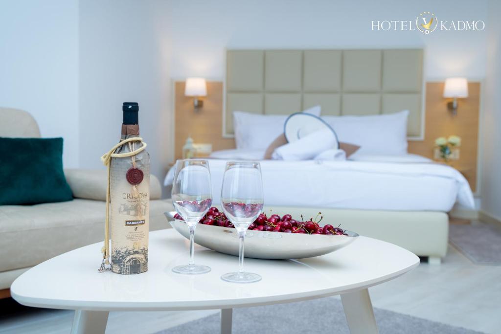 Elegants viesnīcas numurs ar vīna pudeli un glāzēm, kas novietotas uz galda ar ķiršiem, fona gaismām un mājīgu interjeru. Ideāla atmosfēra relaksācijai.